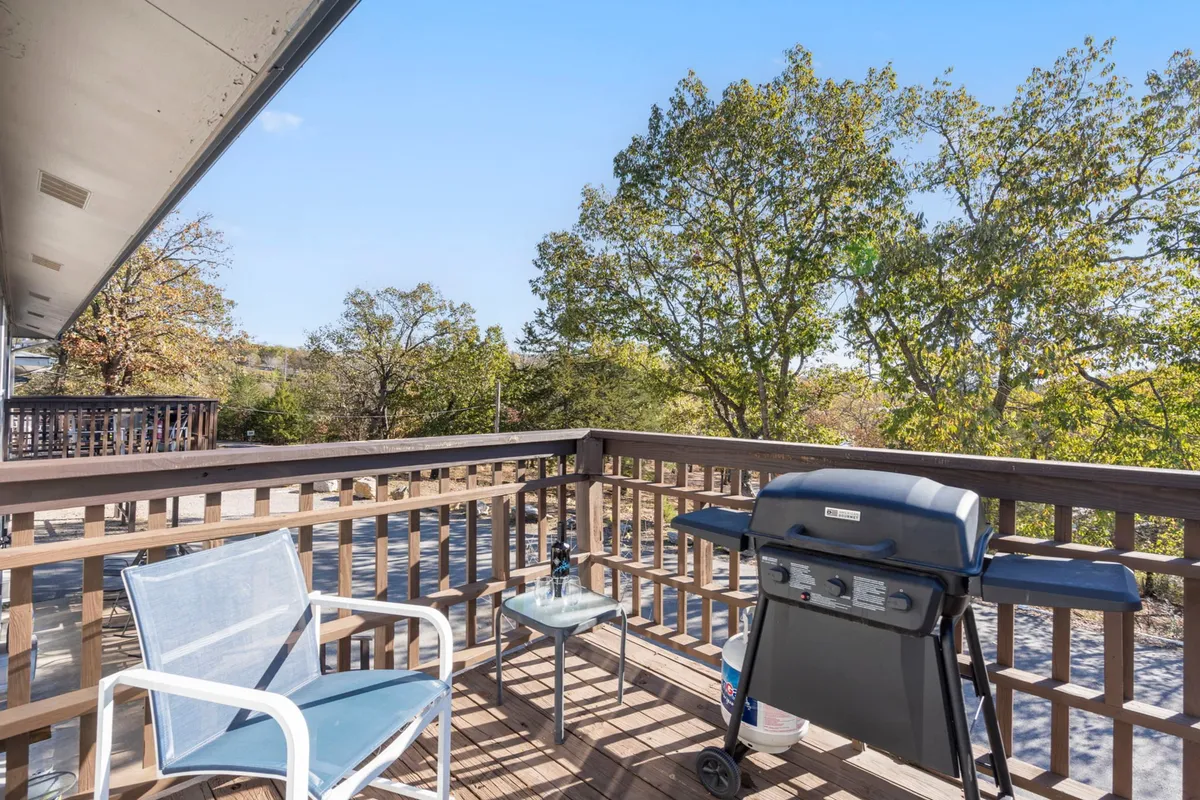 An inviting exterior scene featuring a well-placed grill and comfortable outdoor seating surrounded by mature trees. The setup suggests opportunities for sunset dinners, relaxed morning coffee, and enjoying nature's beauty from a private outdoor space.