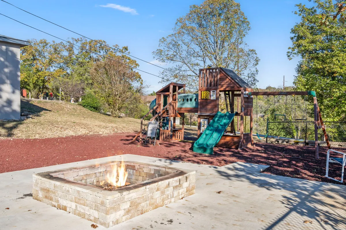 This image features a fire pit surrounded by seating, a vibrant playground with various equipment, and lush greenery in the background. Joyful activity is suggested by the arrangement, making it easy to imagine families gathering, children playing, and groups relaxing or cooking over the fire.