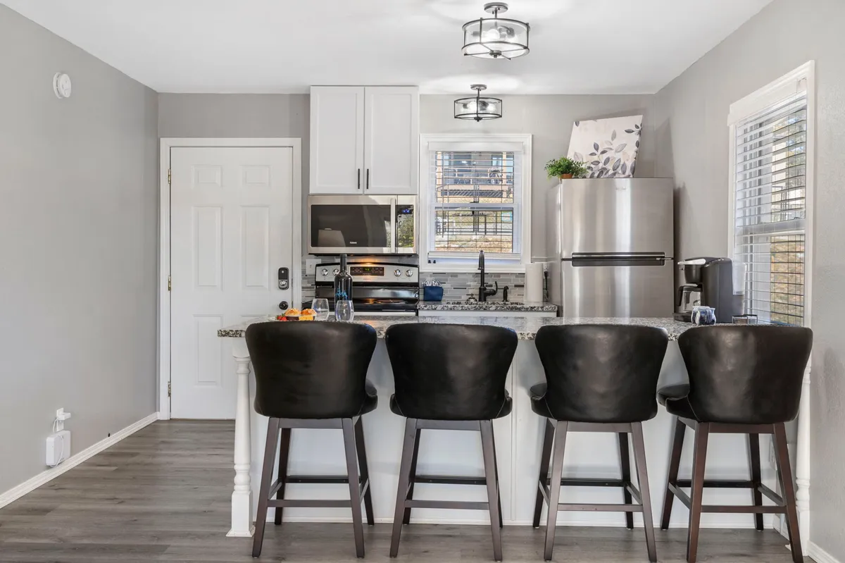 A view of the kitchen area with bar stools at a central island, modern appliances, and a window providing additional natural light. The setup is perfect for preparing meals, socializing, or enjoying casual dining, and the mood is warm and inviting.