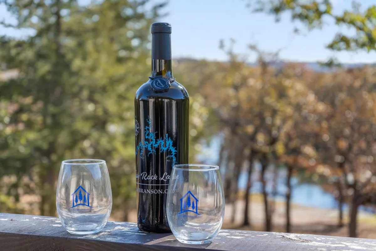 Two wine glasses and a bottle of wine rest on an outdoor table, with a sweeping view of the lake framed in the background. The setting evokes a sense of relaxation at sunset, ideal for sharing drinks and making memories with friends or family by the water.