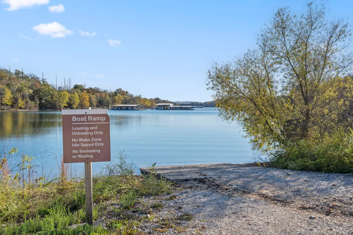 A serene boat ramp leading into the lake, bordered by trees and a peaceful shoreline. The scene features signage and hints at activities such as boating and fishing, with the ramp providing direct, effortless lake access.