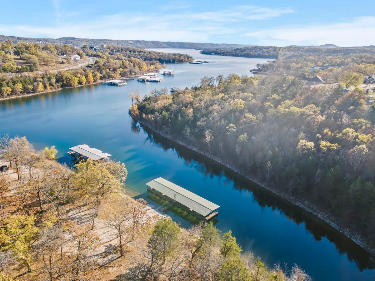 A scenic view of the lake with boat docks extending into the water, surrounded by lush trees. The tranquil water reflects the sky, with hints of distant wildlife and a peaceful natural setting.