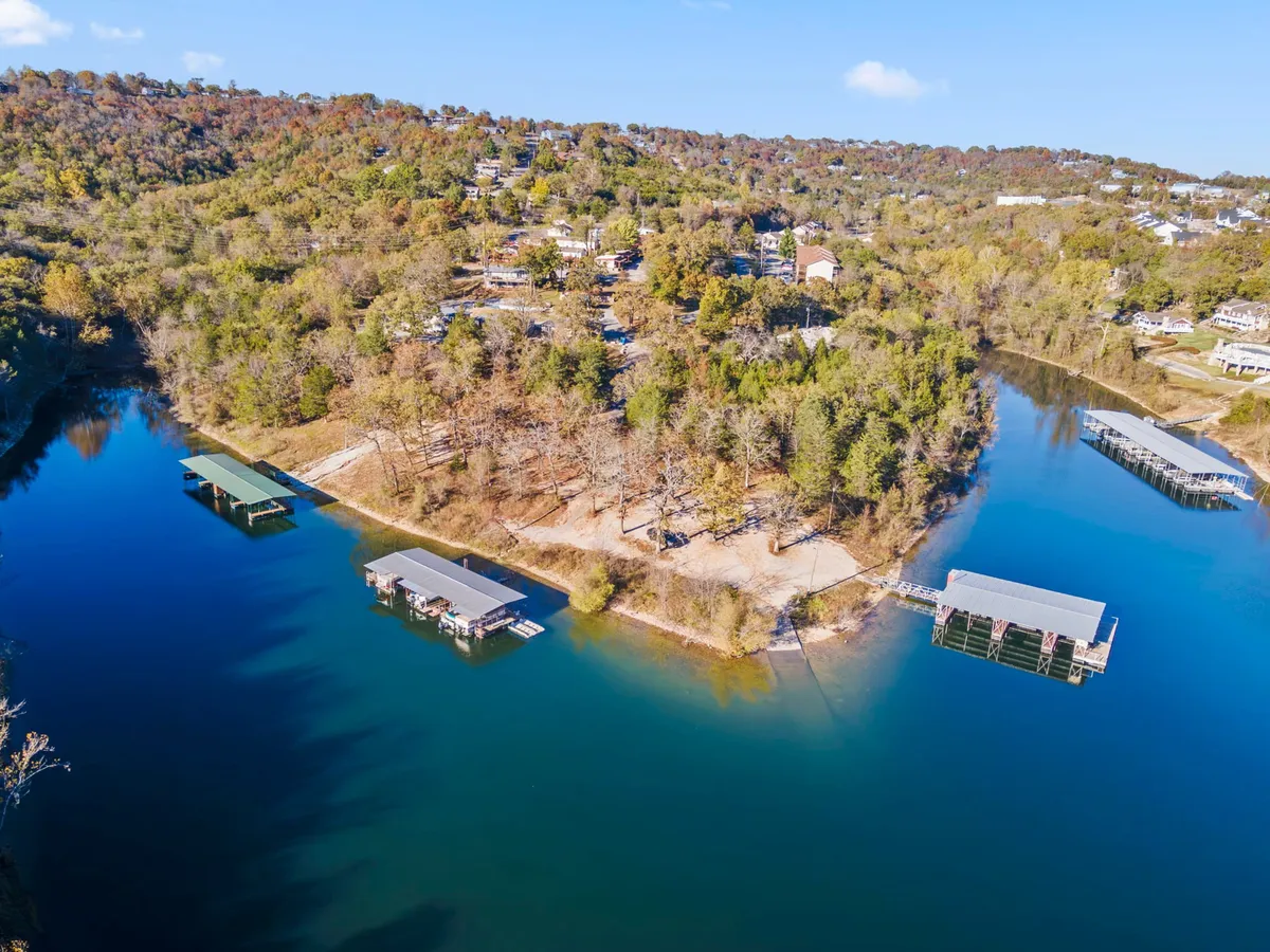 A panoramic exterior view featuring the lake, docks, and wooded shoreline, with hillside homes in the background. The expansive water and hidden coves suggest opportunities for exploration and wildlife viewing.